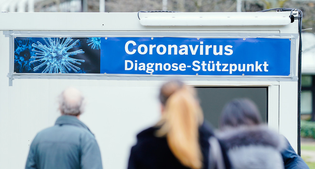Menschen stehen auf dem Gelände des Universitätsklinikums vor speziell für den Test auf den neuartigen Coronavirus aufgestellten Containern, an deren Eingang ein Transparent mit der Aufschrift „Coronavirus Diagnose-Stützpunkt“ angebracht ist.