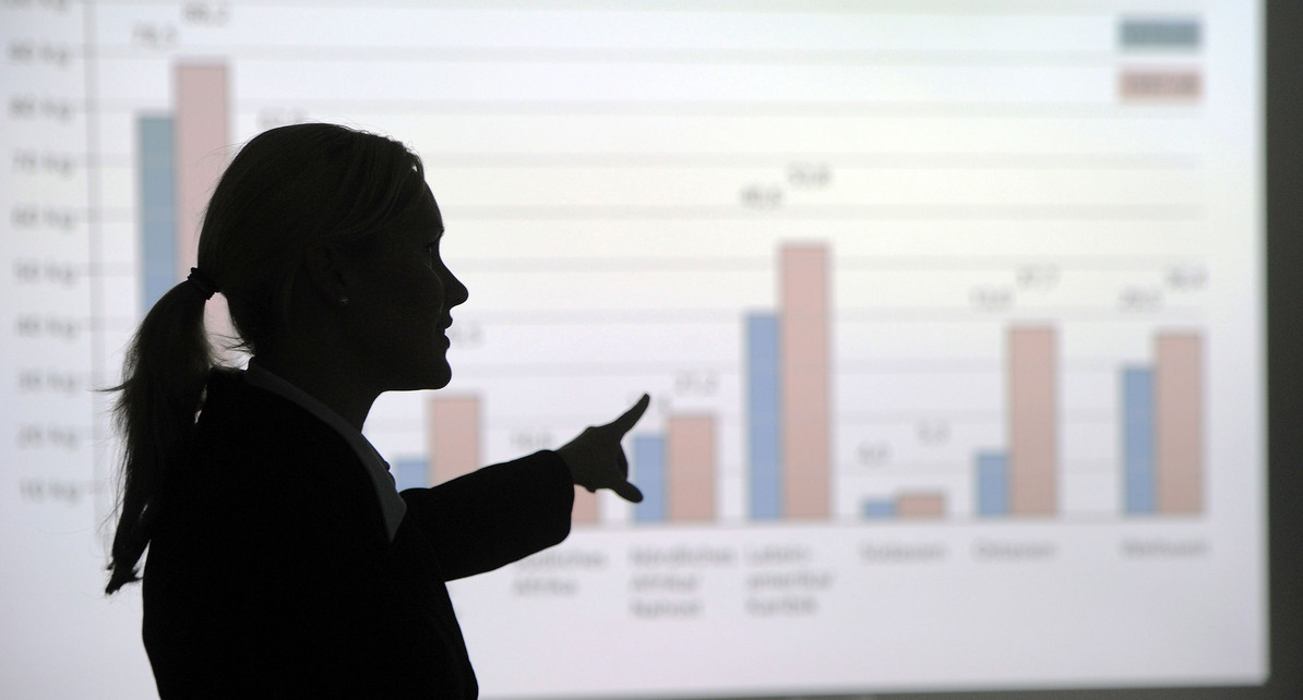 Eine Frau zeigt auf eine Leinwand auf der eine Balkengrafik zu sehen ist (Symbolbild: &copy; dpa).