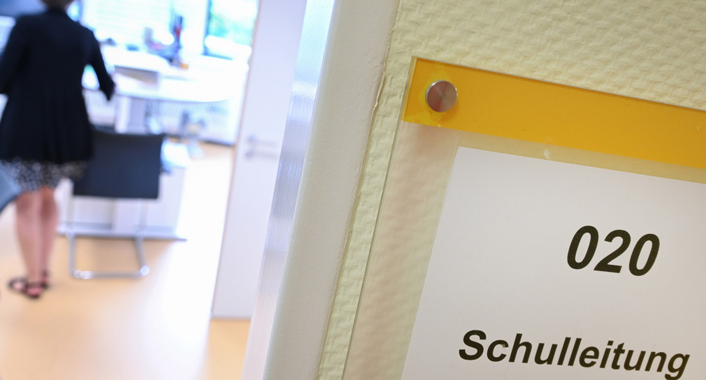 „Schulleitung“ steht auf einem Schild an einer Bürotür, im Hintergrund steht eine Person.