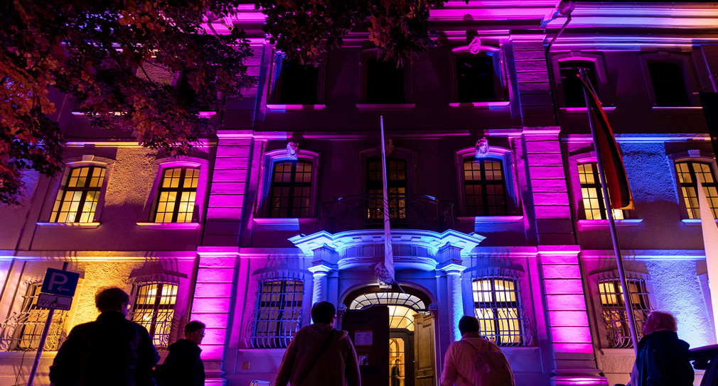 Besucher stehen während der Nacht des offenen Denkmals vor dem bunt angestrahlten Museum für Stadtgeschichte in Freiburg. (Bild: picture alliance/Patrick Seeger/dpa)