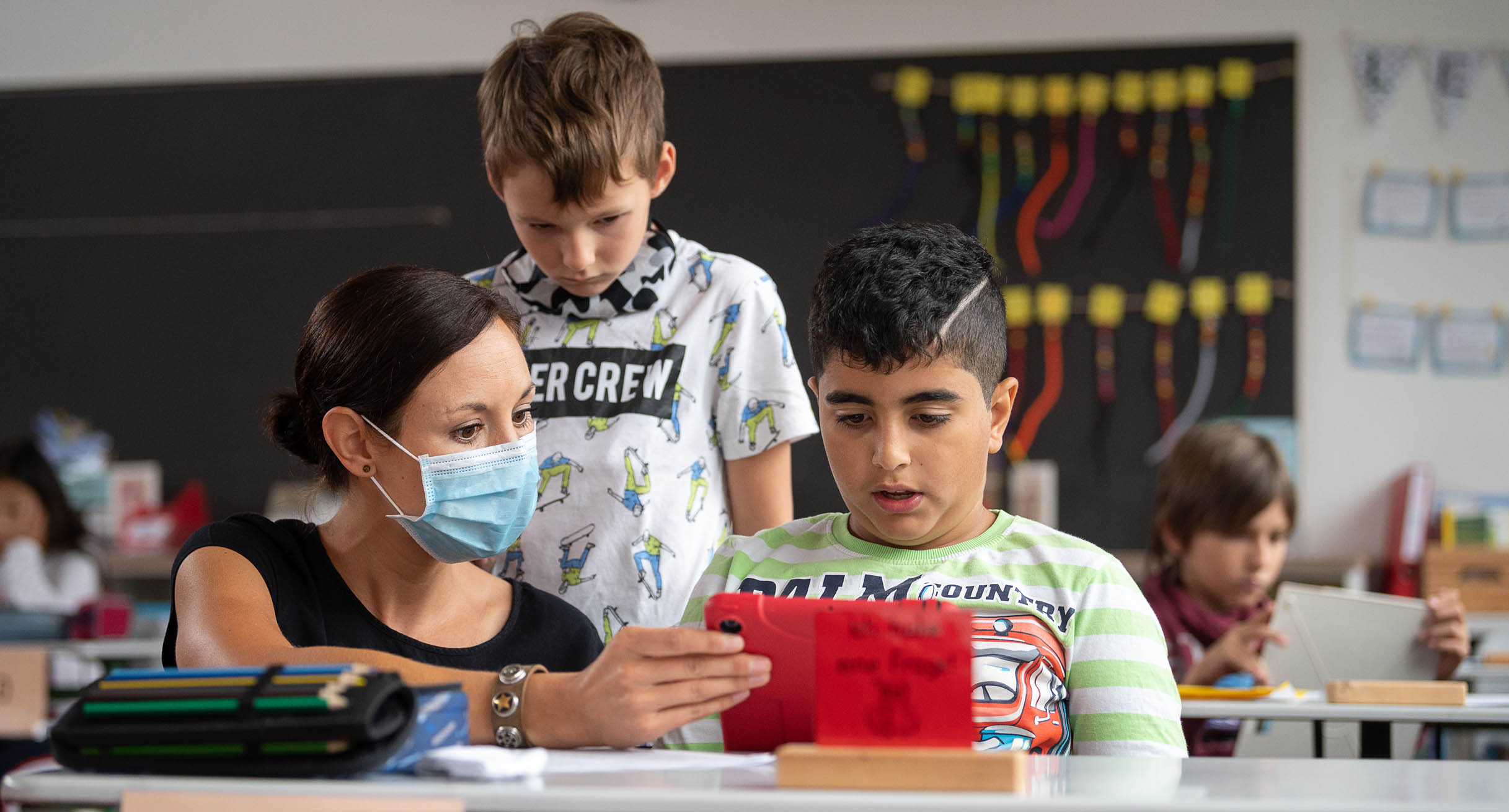 Eine Lehrerin mit Mundschutz gibt zwei Schülern einer Grundschule im Rahmen der sogenannten "Lernbrücken" Nachhilfe.']