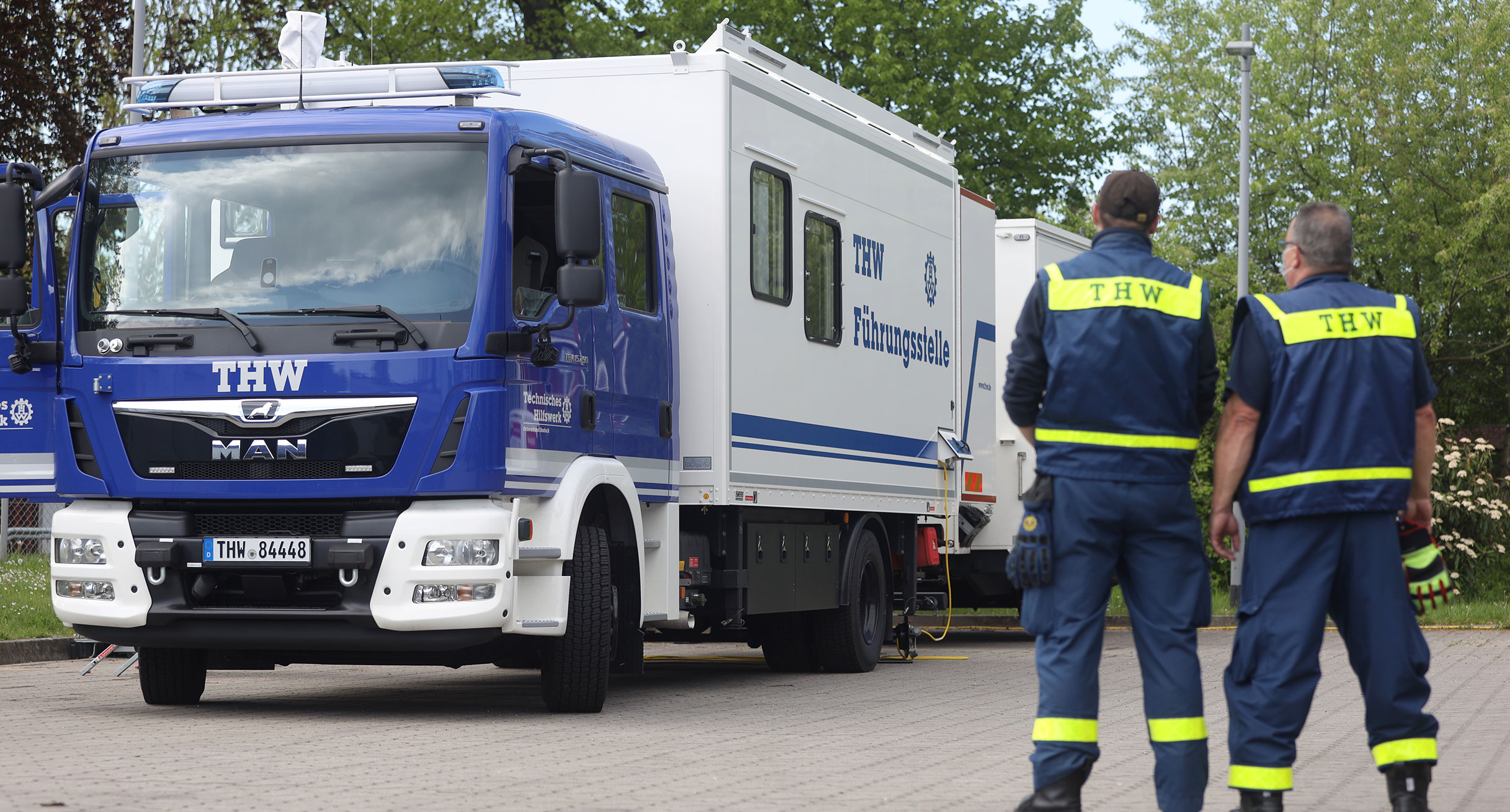 Zwei Mitarbeitende des THW stehen vor einem THW-Einsatzfahrzeug.