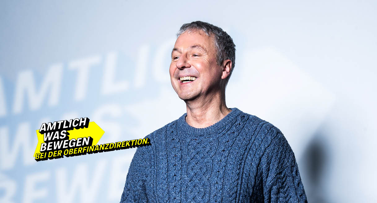 Lächelnder Mann mittleren Alters in einem Strickpullover symbolisiert die Oberfinanzdirektion.