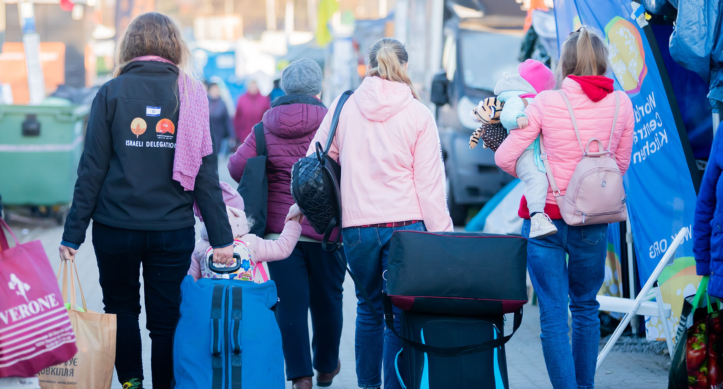 Geflüchtete Frauen und Kinder werden an einem Grenzübergang von einer freiwilligen Helferin begleitet.']