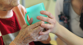Eine Pflegekraft hilft einer alten Frau beim Trinken aus einem Becher in einem Seniorenheim (Bild: Patrick Pleul / dpa)