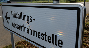 Ein Schild mit der Aufschrift &bdquo;Fl&uuml;chtlingserstaufnahmestelle&ldquo;, im Hintergrund ein Fahrzeug an einer Einfahrt.