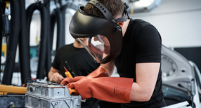 Ein Sch&uuml;ler mit Schutzbrille und Handschuhen in einer Autowerkstatt