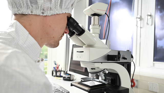 Ein Ingenieur kontrolliert in einem Labor mit einem Mikroskop einen Chip zum Einsatz in einen Quantencomputer.