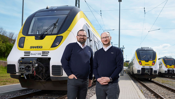 Zwei Lokführer stehen am Kopf eines Zuges der SWEG und lachen in die Kamera.