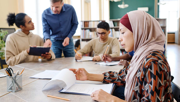 Eine muslimische Einwanderin sitzt mit anderen Personen am Tisch und schaut sich während des Englischunterrichts Blätter mit Grammatikaufgaben an.
