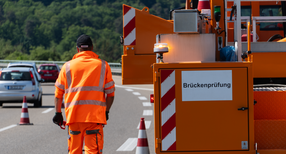 Ein Stra&szlig;enw&auml;rter mit orangenen Klamotten l&auml;uft auf einer Br&uuml;cke.