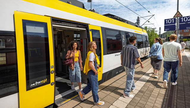 Junge Menschen steigen aus einem Zug am Bahnsteig aus.