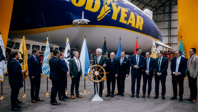 Die IBK-Regierungschefs bei der symbolischen Steuerrad&uuml;bergabe im Zeppelin-Hangar Friedrichshafen, im Hintergrund steht ein Zeppelin.