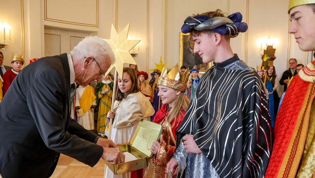 Ministerpr&auml;sident Winfried Kretschmann (links) &uuml;berreicht den Sternsingerinnen und Sternsingern eine Geldspende.