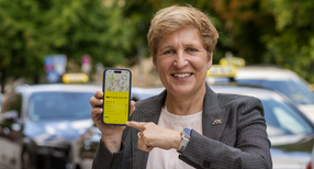 Verkehrsministerin Razavi steht neben Autos mit einem Handy in der Hand.