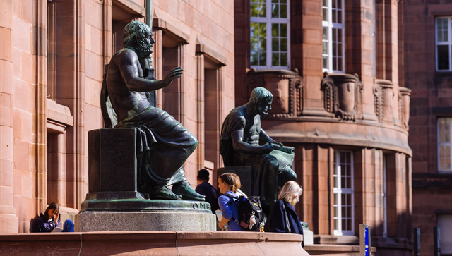 Skulpturen von Homer (links) und Aristoteles stehen vor dem Haupteingang des Kollegiengeb&auml;ude I (KG1) der Universit&auml;t Freiburg w&auml;hrend Menschen dazwischen hindurchgehen.