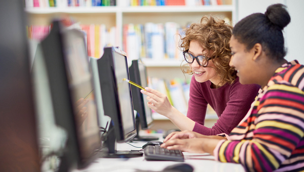 Zwei junge Frauen zeigen auf den Monitor und diskutieren gemeinsam über die Präsentation am Computer.