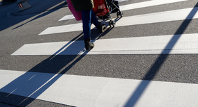 Eine Mutter geht mit einem Kinderwagen &uuml;ber einen Zebrastreifen.