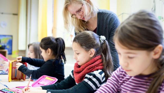 Eine Lehrerin in der Grundschule mit Sch&uuml;lerinnen und Sch&uuml;lern.