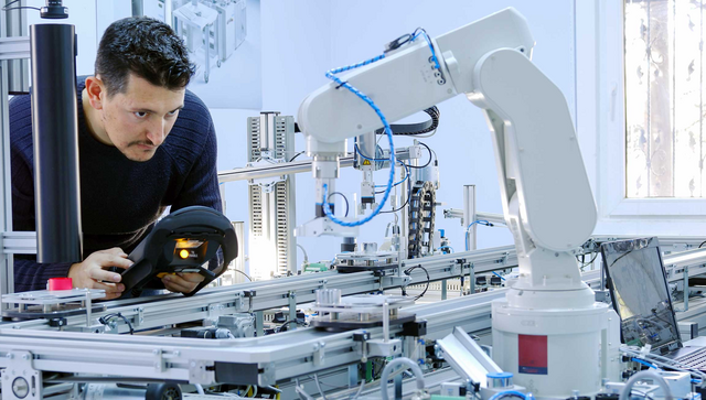 Ein Mann programmiert einen Roboterarm, der in einer Produktionslinie einer Smart Factory eingebaut ist.