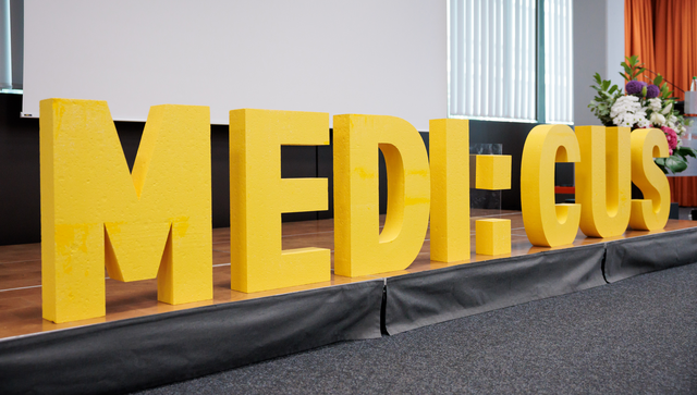Schriftzug &bdquo;MEDI:CUS&ldquo; auf einer B&uuml;hne