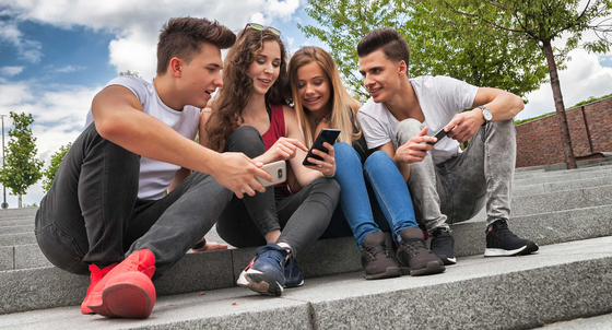 Vier Jugendliche sitzen auf einer Freitreppe und betrachten etwas auf dem Smartphone