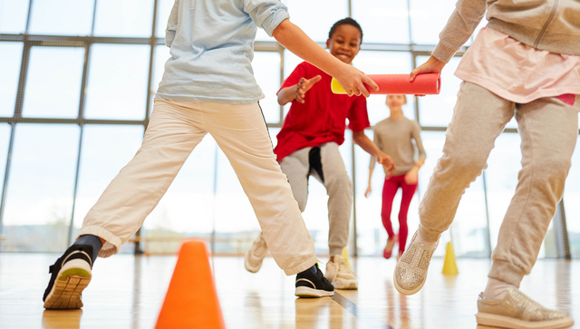 Ein Kinderteam macht einen Staffellauf im Sportunterricht in der Turnhalle.