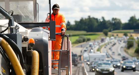 Ein Bauarbeiter bedient eine große Baumaschine auf einer Autobahnbaustelle. (Bild: © dpa)