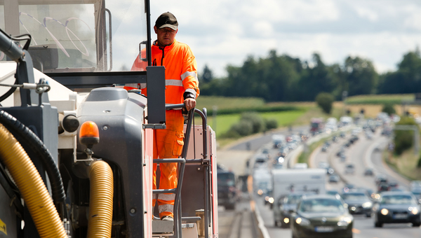 Ein Bauarbeiter bedient eine große Baumaschine auf einer Autobahnbaustelle. (Bild: © dpa)