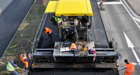Bauarbeiter erneuern den Fahrbahnbelag auf einer Stra&szlig;e.