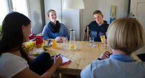 In einer Wohngemeinschaft sitzen Studierende um den K&uuml;chentisch und unterhalten sich.