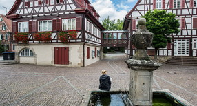 Symbolbild: Eine Frau sitzt an einem Dorfbrunnen. (Foto: &copy; dpa)