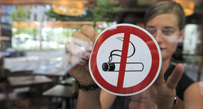 Eine Frau befestigt einen &bdquo;Rauchen-Verboten&ldquo;-Aufkleber an einer Scheibe (Bild: &copy; dpa).